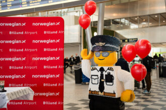 A LEGO figure next to a Billund Airport and Norwegian signboard.