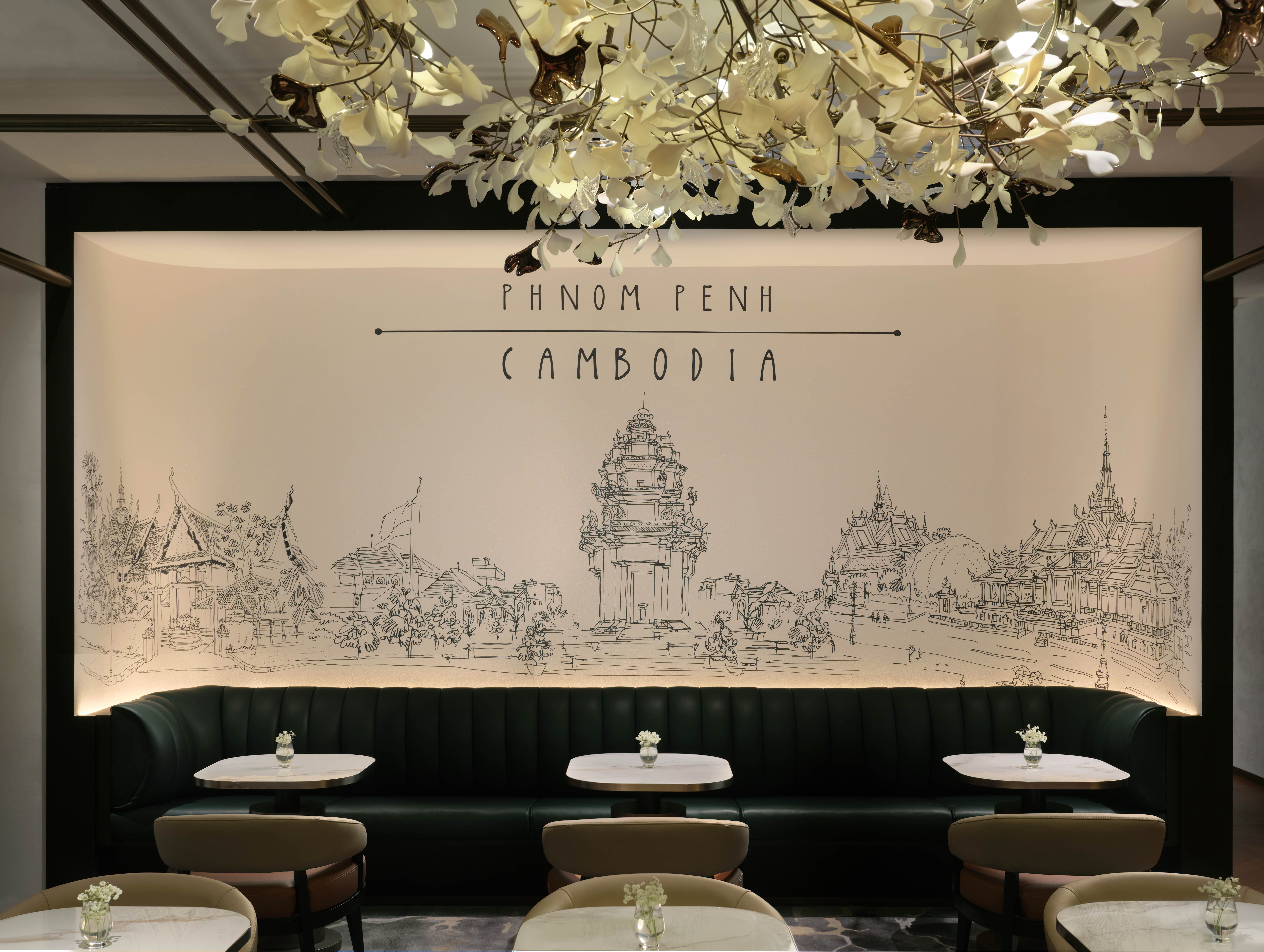 A wall with an illustration of the Phnom Penh skyline behind tables and chairs for dining.