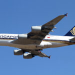 A Singapore Airlines plane flying high above the ground with a blue sky in the background.