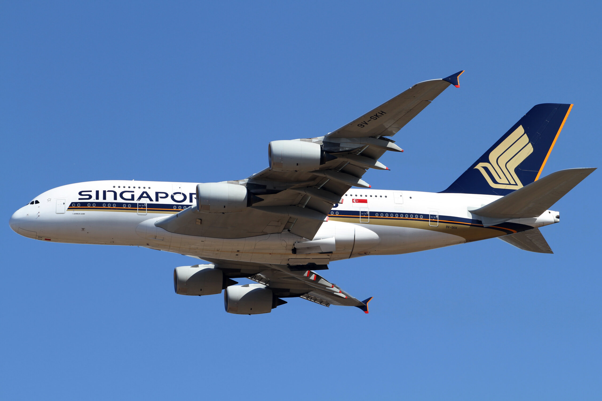 A Singapore Airlines plane flying high above the ground with a blue sky in the background.