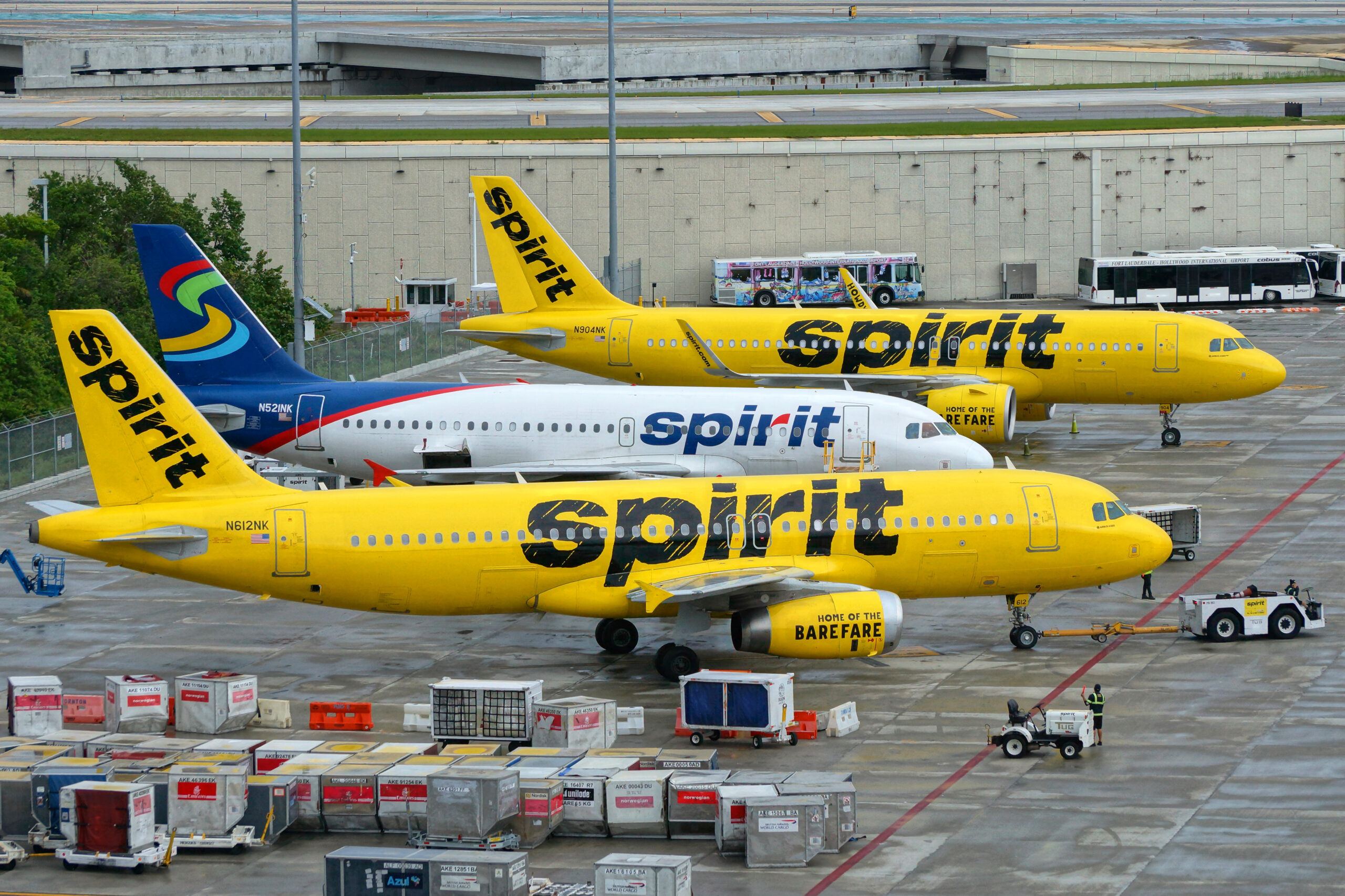 Three Spirit Airlines planes lined up on the tarmac, two in bright yellow and one in blue and white.