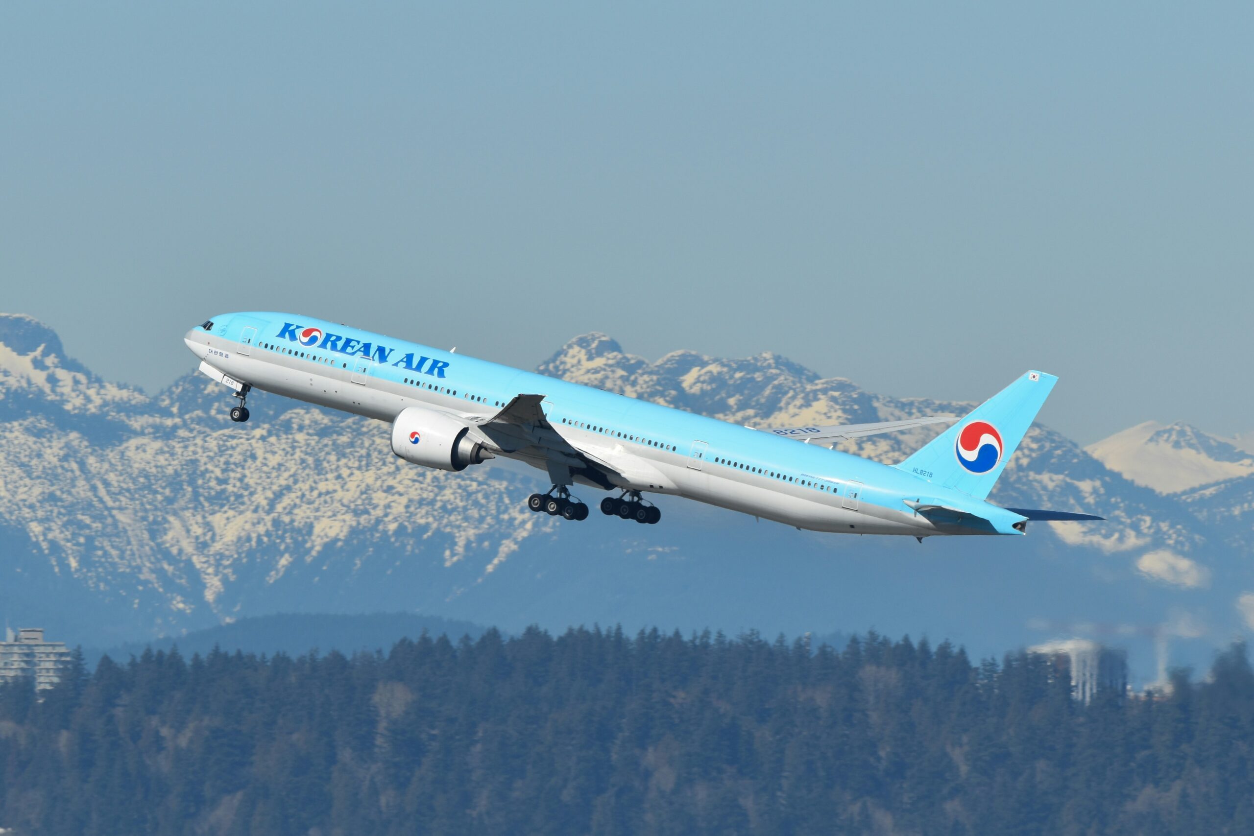 A Korean Air plane departing Vancouver with snowy mountains in the background.