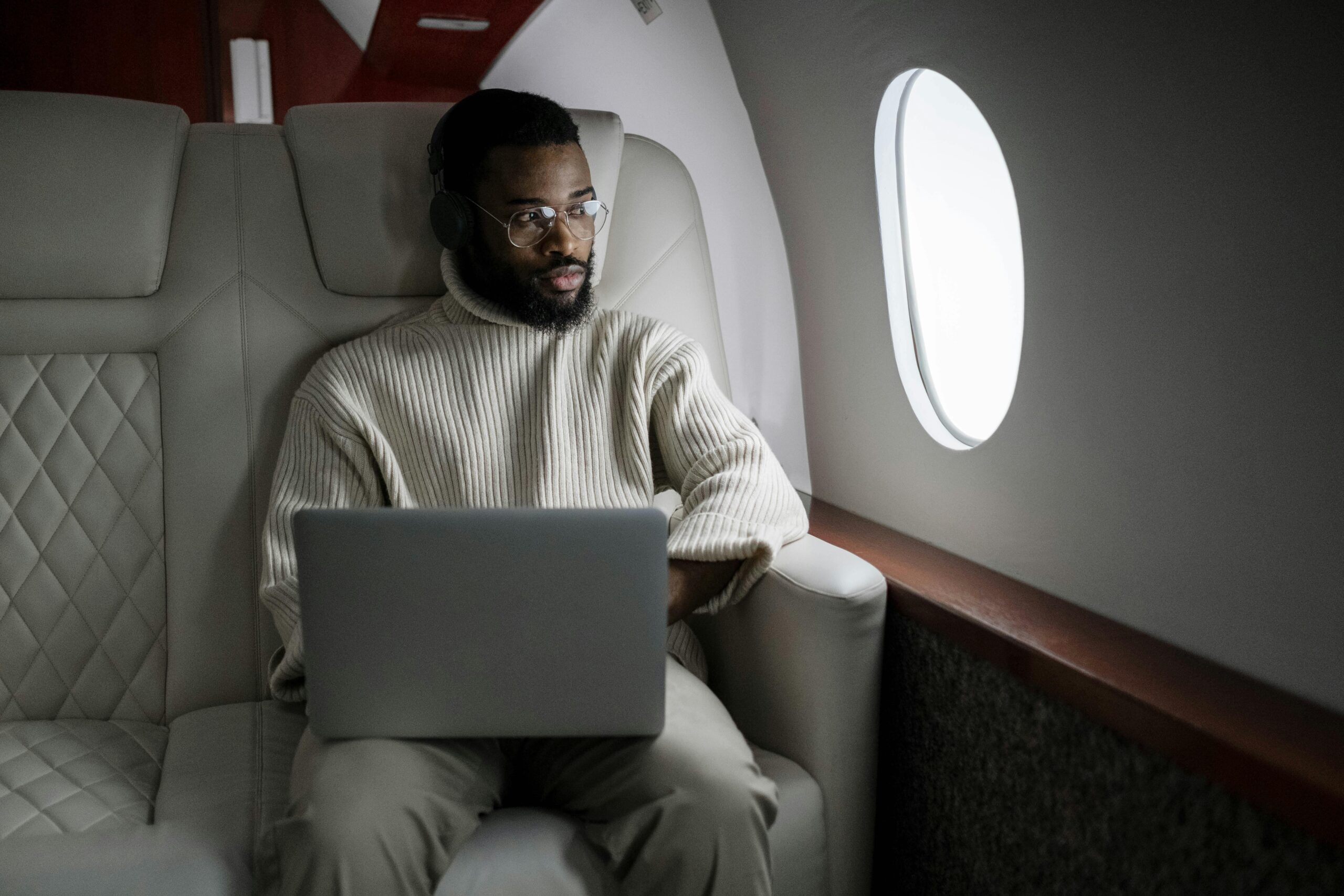 Man in White Sweater Sitting on a Plane Using Macbook
