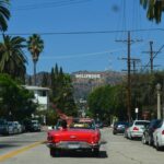 A red car driving on a road with the Hollywood sign in the background