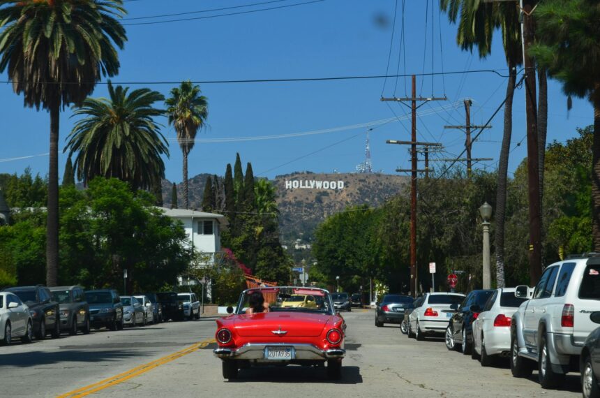A red car driving on a road with the Hollywood sign in the background