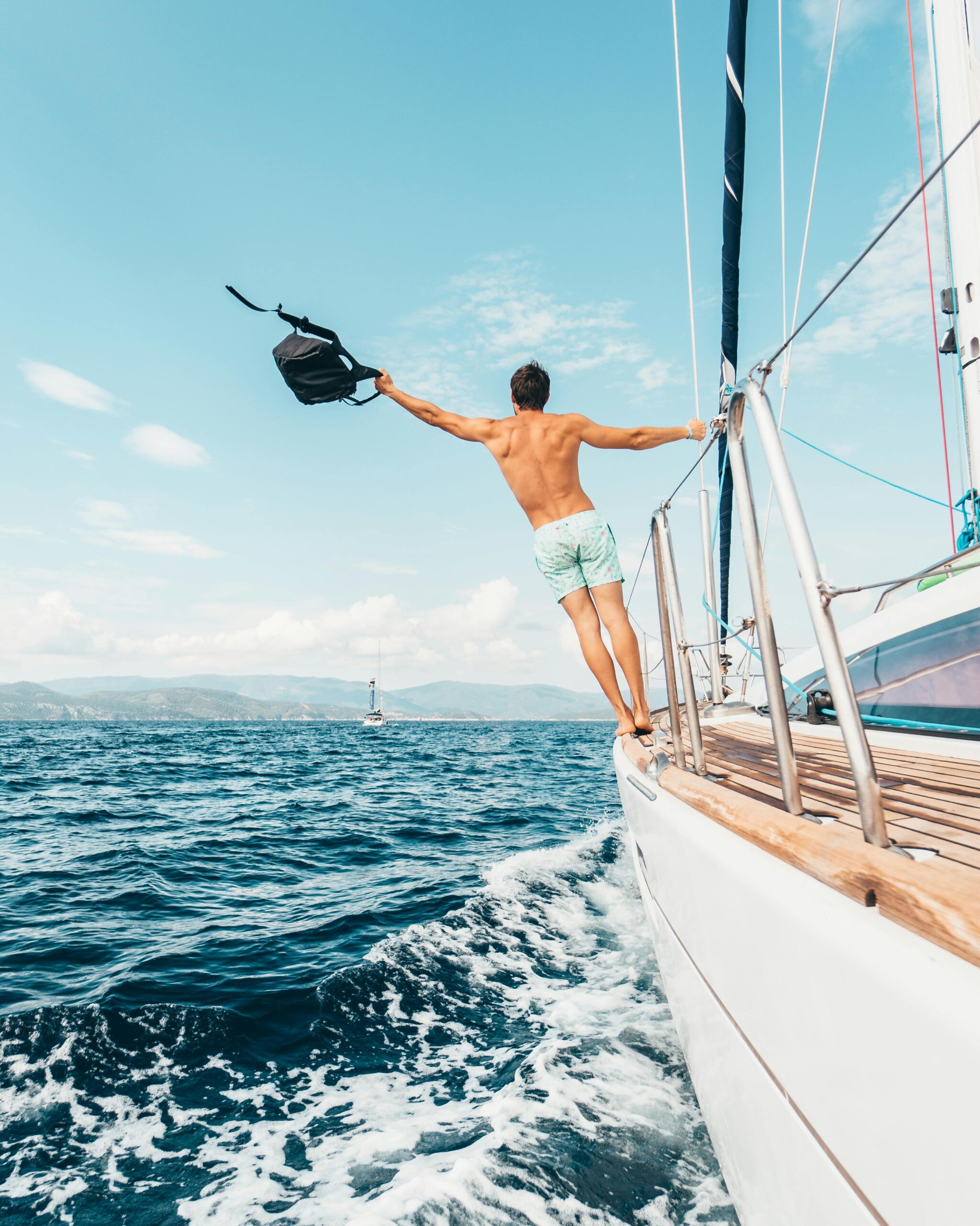 Man holding a backpack standing on the edge of a boat on the sea