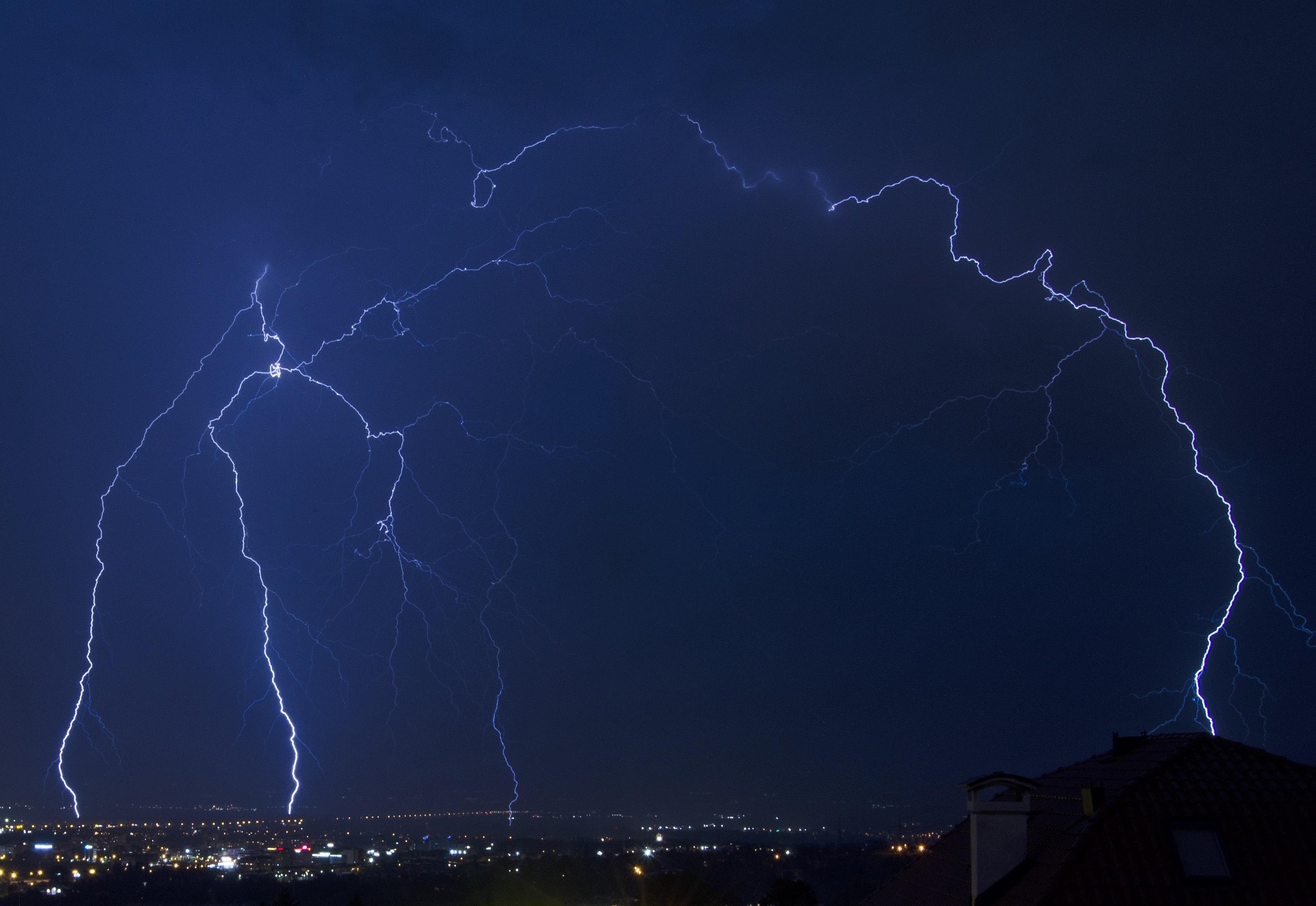 Night blue sky over a city with a massive lightning bolt striking, illustrating lightning safety and dramatic lightning activity.