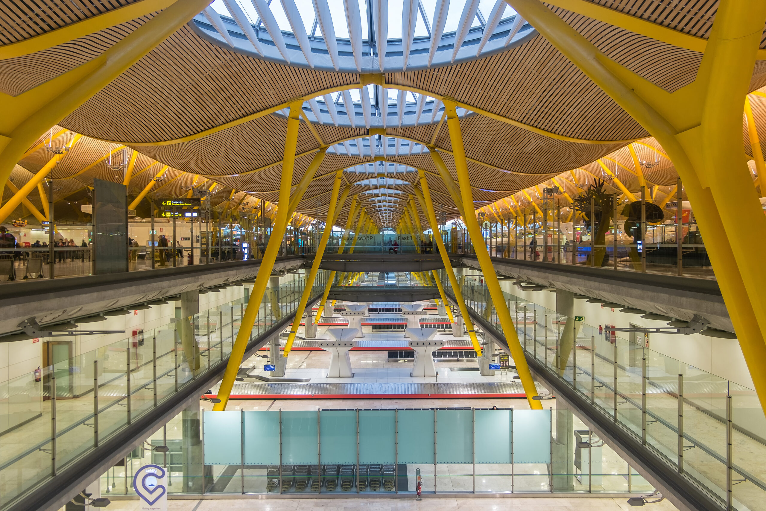 A picture from inside Madrid Barajas airport, with yellow and wood accents holding up the curved roof.