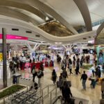 The terminal of Zayed International Airport, Abu Dhabi, with many people and duty free shops spread across the hall.