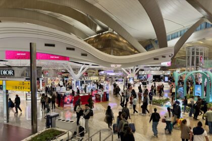 The terminal of Zayed International Airport, Abu Dhabi, with many people and duty free shops spread across the hall.