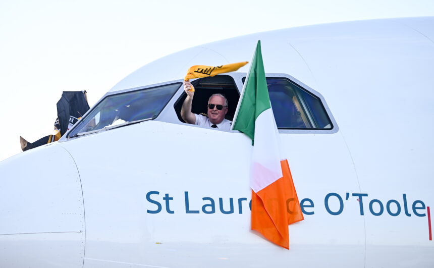 Aer Lingus pilot waves from cockpit window beside Irish flag on aircraft St Laurence O’Toole, symbolising Aer Lingus pilots during ongoing Aer Lingus industrial relations and pilot dispute.