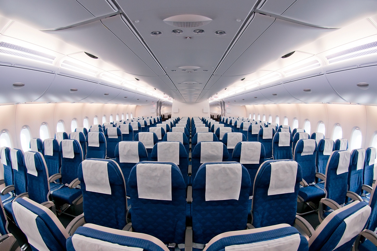 The inside of a Korean Air A380, with blue seats and white seat coverings lining the aisles.