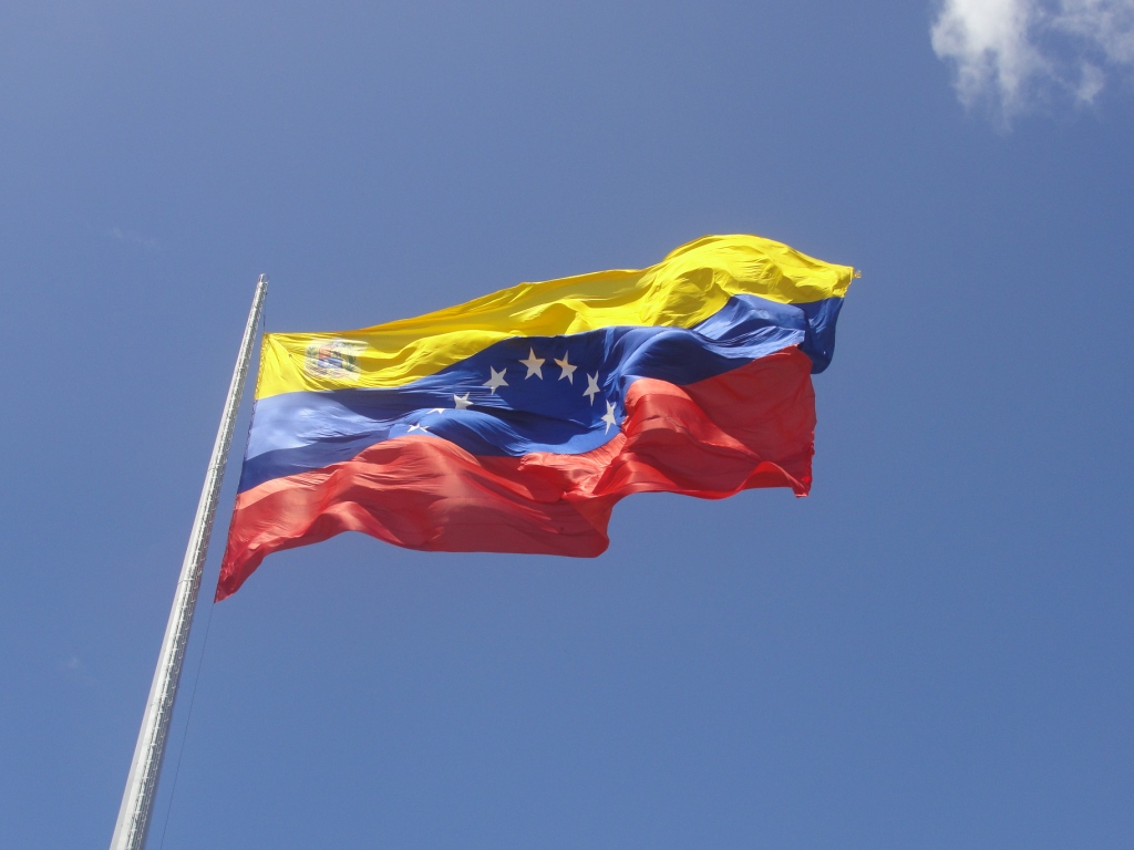 Venezuelan flag flying against a blue sky illustrating the Venezuela aviation ban, tightened Venezuela airspace, rising U.S.-Venezuela tensions, Venezuela airline restrictions 2025, and aviation used as political leverage.
