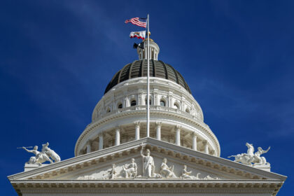 Close-up view of the California State Capitol dome with the U.S. and California flags flying above, symbolising government decisions affecting the U.S. government shutdown and national aviation crisis.