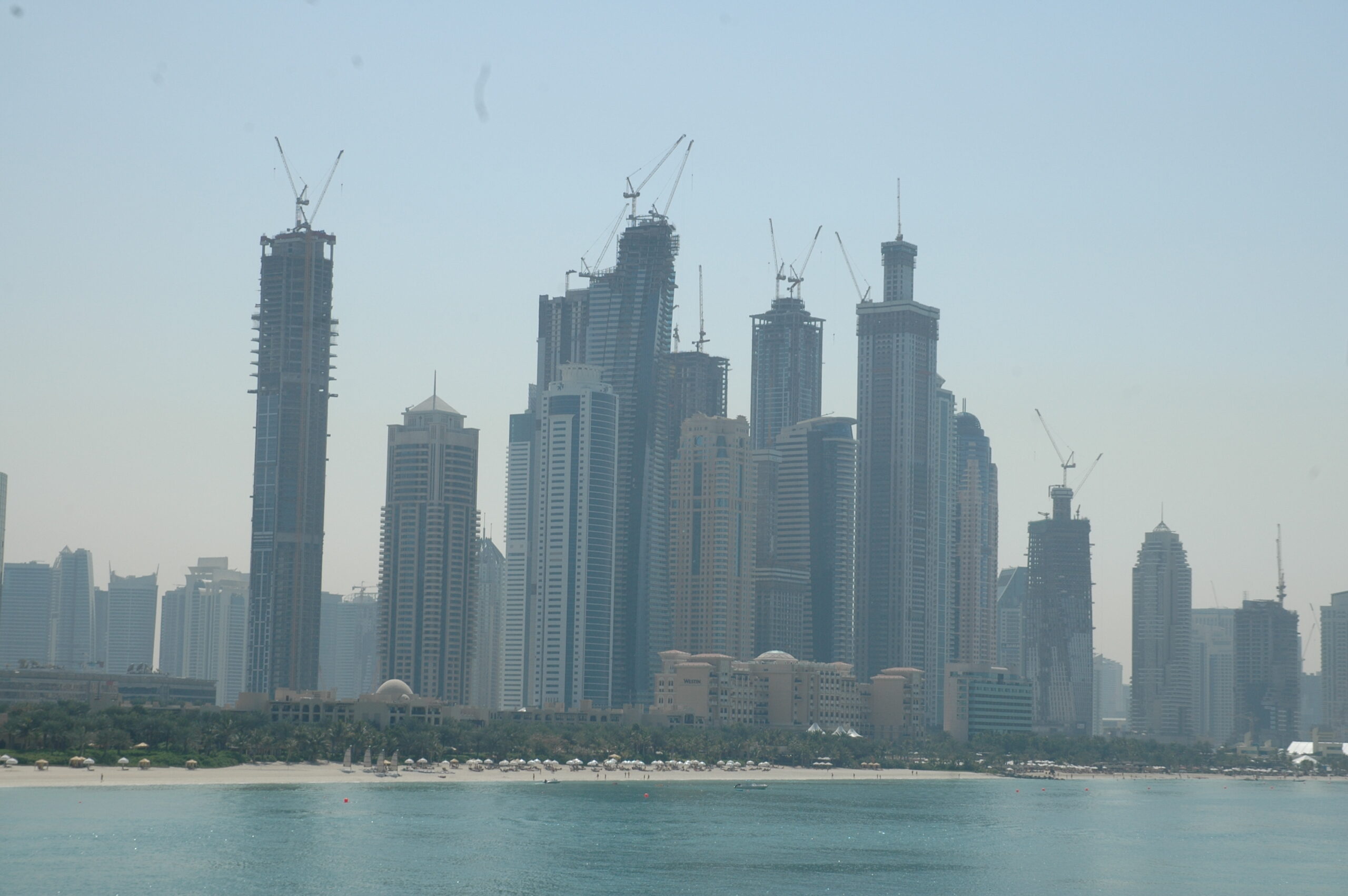 The Dubai skyline with multiple high rise buildings, all with cranes on top of them.