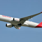 An Iberia plane flying high up in a blue sky.
