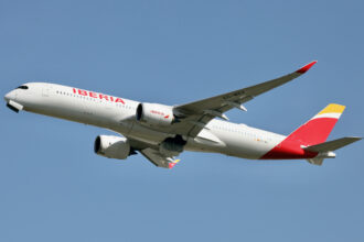 An Iberia plane flying high up in a blue sky.