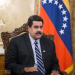 Nicolás Maduro seated in front of the Venezuelan flag during a government meeting, illustrating the Venezuela aviation ban, tightened Venezuela airspace controls, rising U.S.-Venezuela tensions, Venezuela airline restrictions 2025, and aviation used as political leverage.