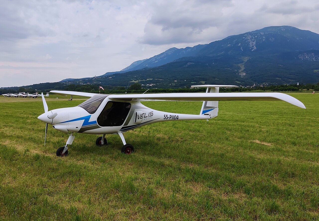 A small aircraft pn the grass with mountains in the background 