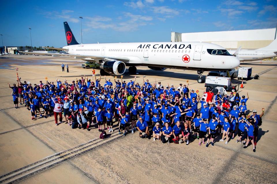 A huge group photo of Dreams Take Flight posing with a Air Canada aircraft behind them