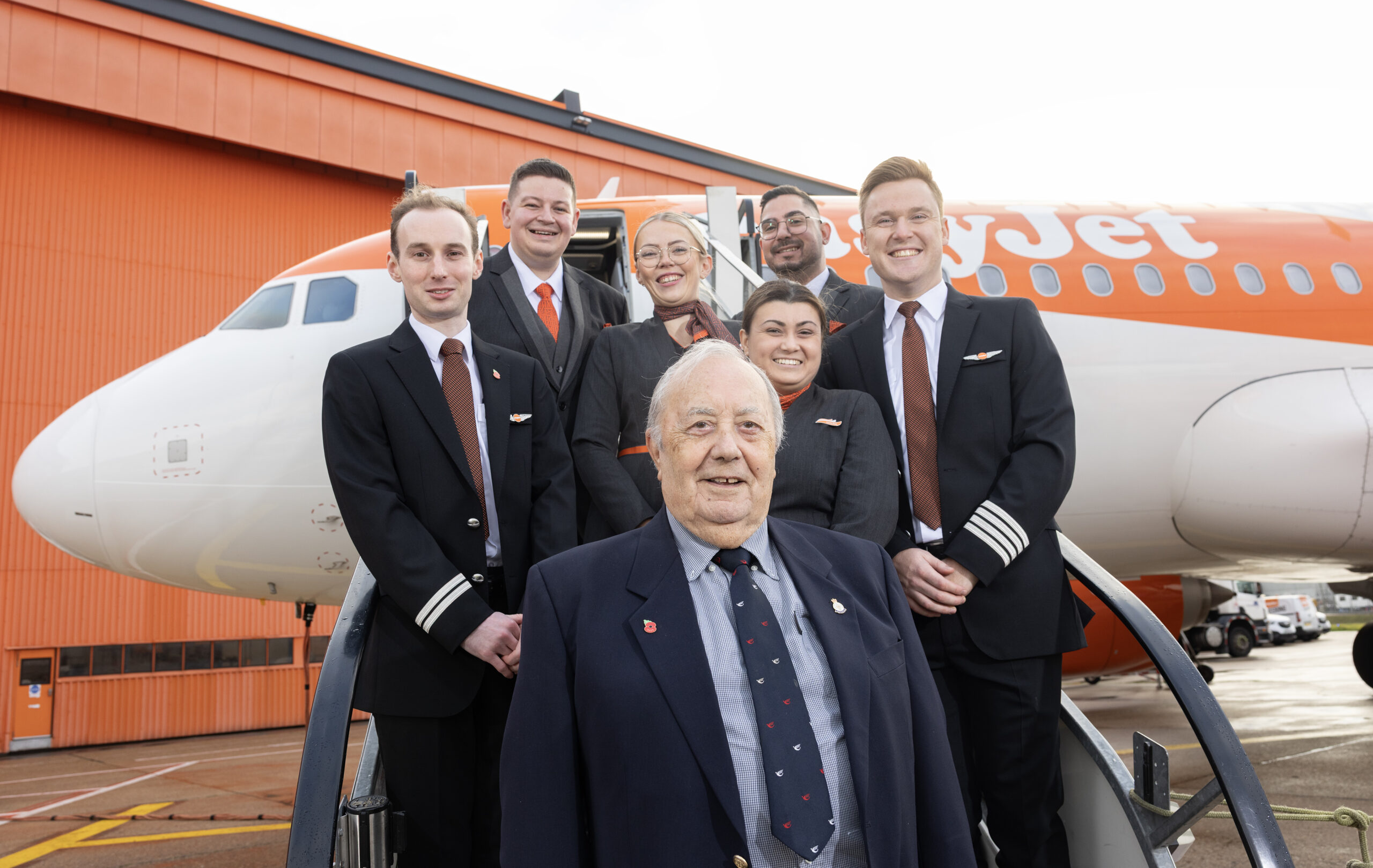 A group of flight attendants and a retired air captain, Fred Rivett, pose for a picture in front of an aircraft.