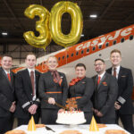 A group of flight attendants stand in front of an orange easyJet aircraft with balloons reading "30".