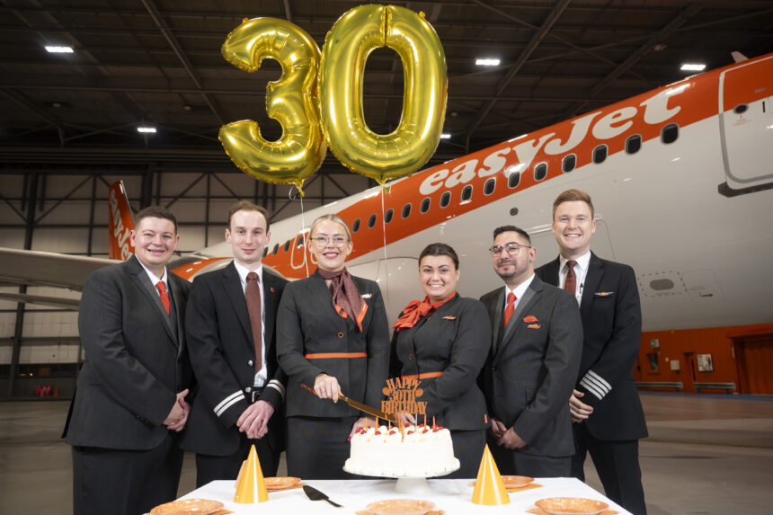 A group of flight attendants stand in front of an orange easyJet aircraft with balloons reading "30".