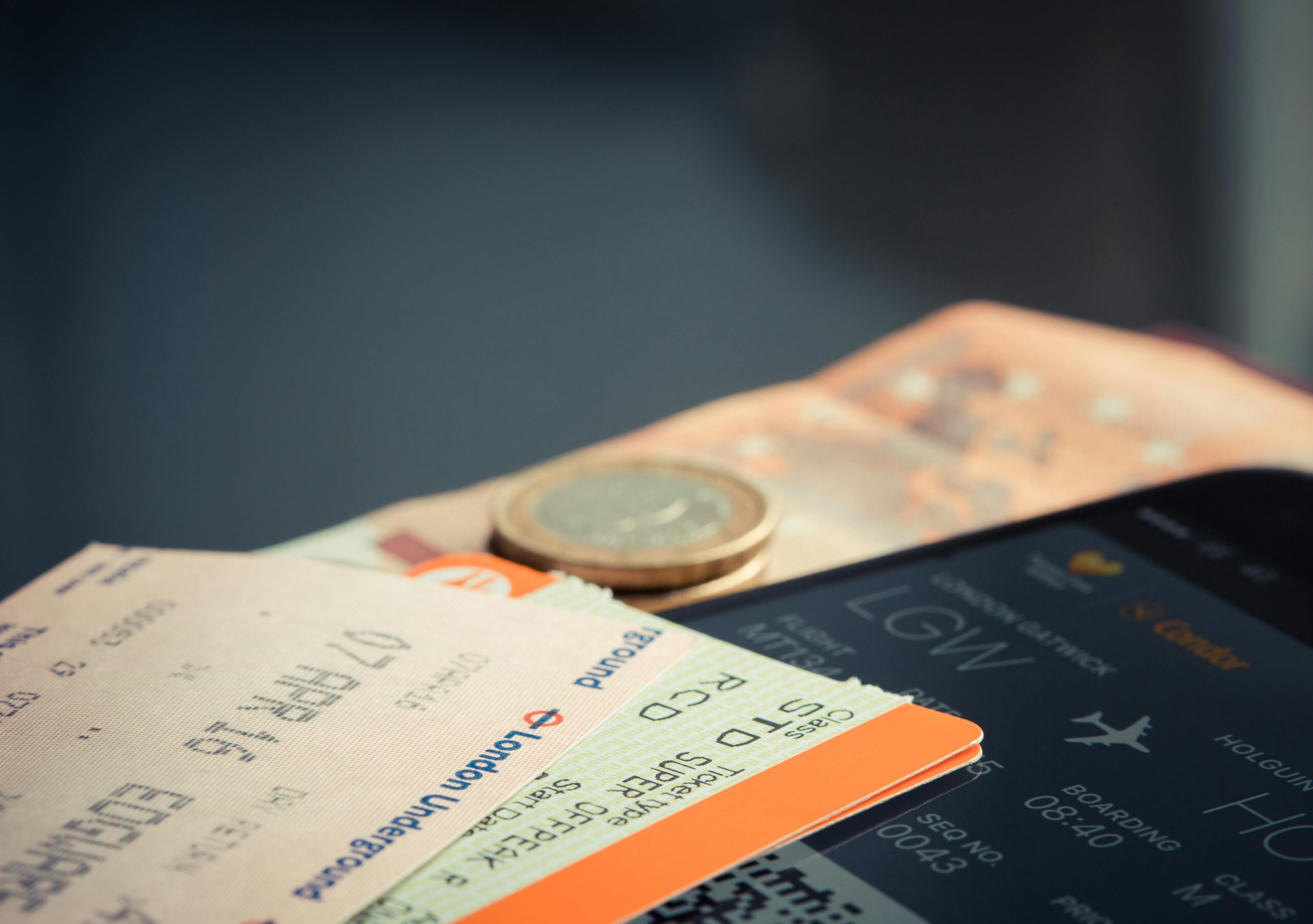 Digital plane ticket on the phone, London Tube and train tickets next to some cash