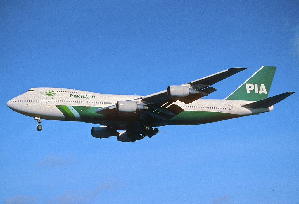 PIA aircraft flying in the air, with green and white livery against a bright blue sky.