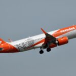 An orange and white easyJet aircraft with special NEO livery takes off.