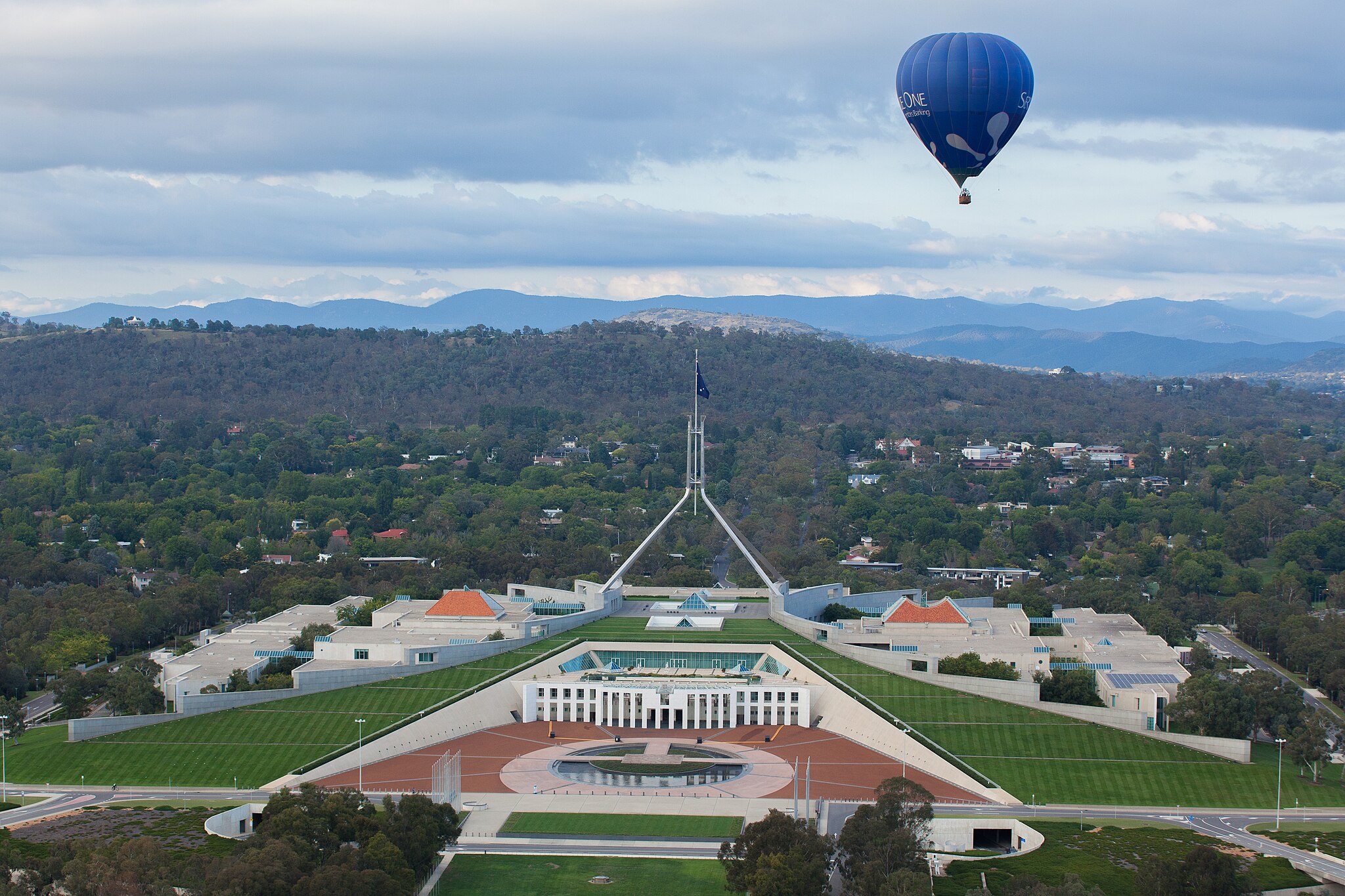 Parliament House in Canberra, surrounded by woods and with a hot air balloon in the sky.