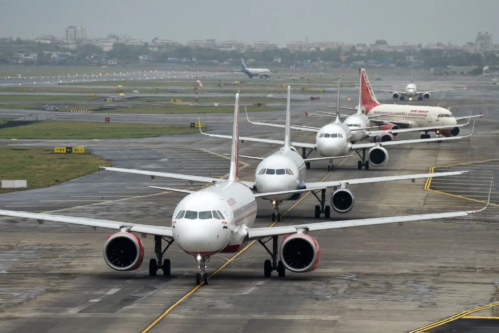 Multiple aircraft lined up on the tarmac at Mumbai airport, waiting for takeoff under gray skies