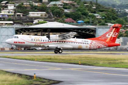 A side profile of an Air Tahiti ATR 72-600 turboprop aircraft landing on a runway. The plane features a special white and red livery with "60 ANS YEARS" gold lettering on the fuselage and intricate Polynesian-inspired patterns on the tail. A lush green hillside dotted with residential houses is visible in the background under an overcast sky.
