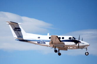 A twin-engine turboprop aircraft serving as a Civilian Air Ambulance for St Luke's flies in the blue sky.