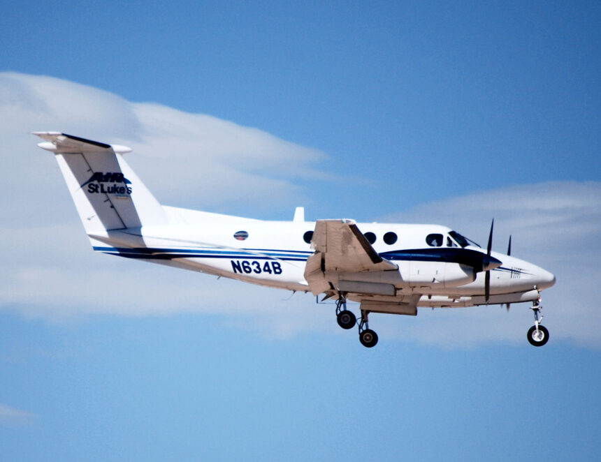 A twin-engine turboprop aircraft serving as a Civilian Air Ambulance for St Luke's flies in the blue sky.