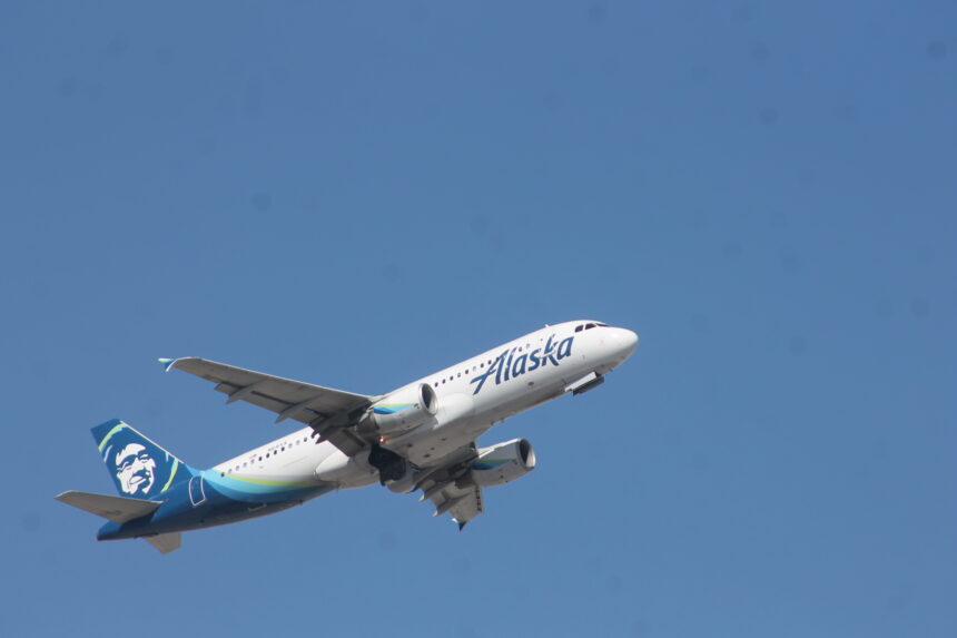 An Alaska Airlines Airbus A320 flies in the blue sky.