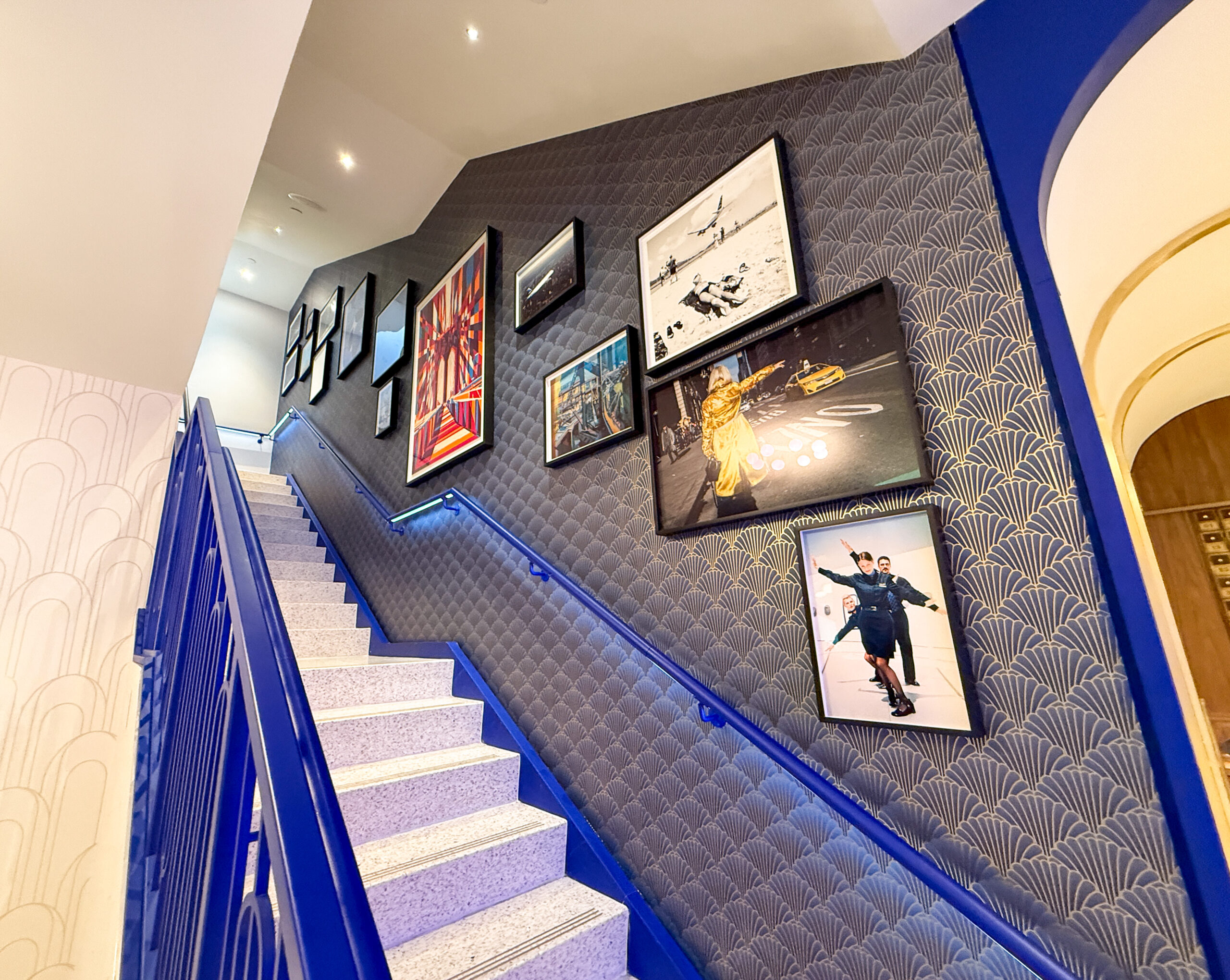 Electric blue and white stairs are lined by a wall with many different framed pictures representing New York, including iconic yellow taxis.