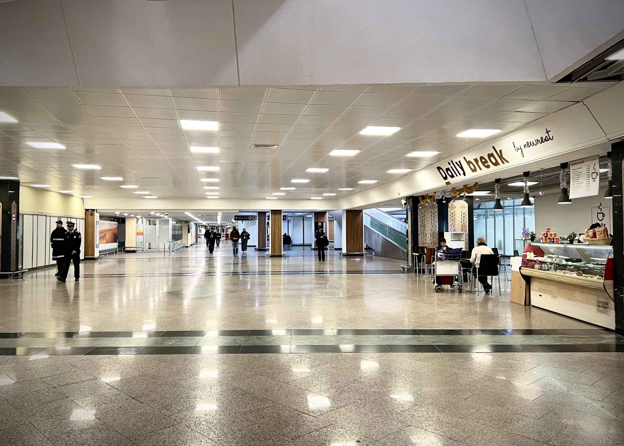 Interior of the Casablanca Mohammed V International Airport, with a Daily Break coffee shop on the right and some people walking. 