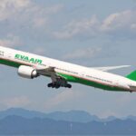 EVA Air Boeing 777-300ER in flight against a blue sky, featuring green accents on the livery.