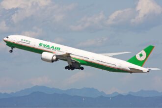 EVA Air Boeing 777-300ER in flight against a blue sky, featuring green accents on the livery.