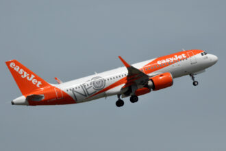 An easyJet Airbus A320neo flies in the grey sky.