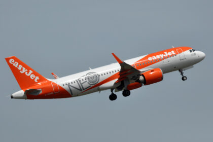 An easyJet Airbus A320neo flies in the grey sky.