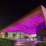 A night time exterior picture of the Exhibition centre in Bahrain. With its flat roof and purple lights showing underneath.
