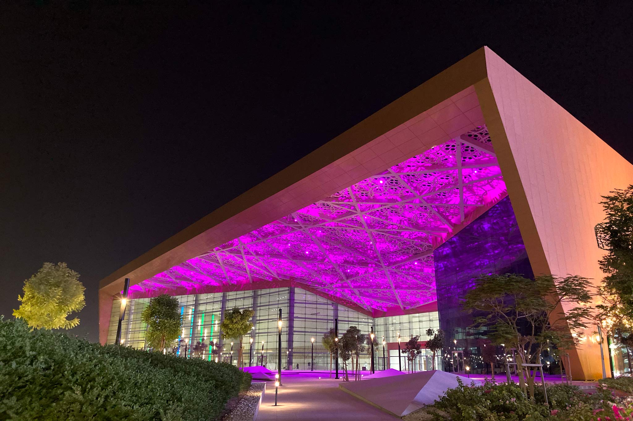A night time exterior picture of the Exhibition centre in Bahrain. With its flat roof and purple lights showing underneath.
