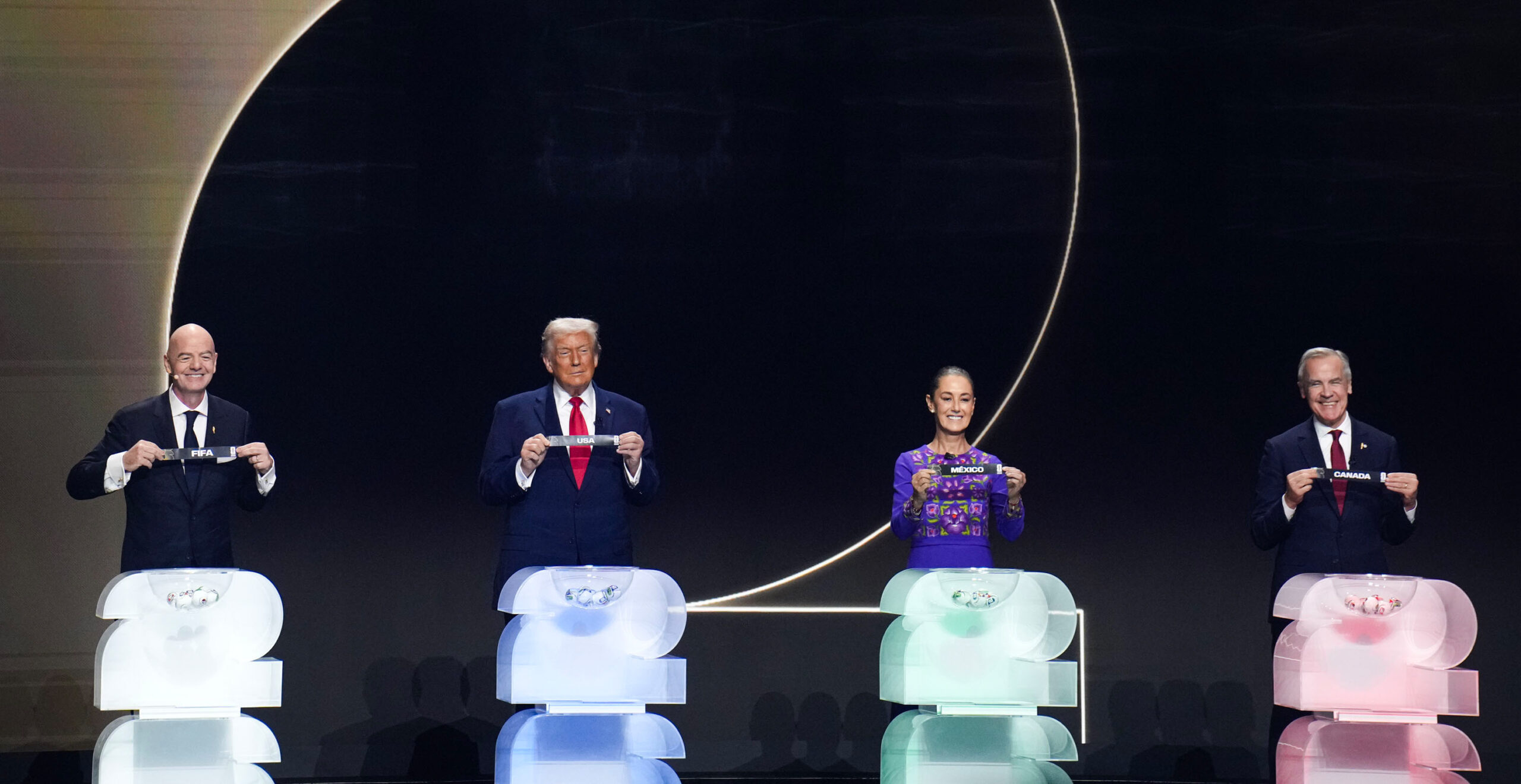 From left, FIFA President Gianni Infantino, U.S. President Donald Trump, Mexico President Claudia Sheinbaum and Canada Prime Minister Mark Carney hold small banners with their countries' names – FIFA in the case of Infantino. 