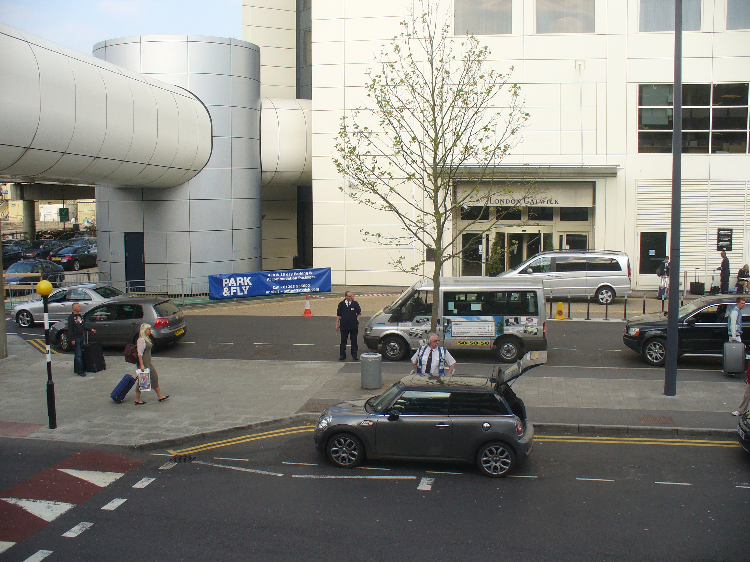 The exterior of London Gatwick Airport showing cars, and people outside the airport.