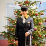 Lufthansa Cabin Crew standing in front of a Christmas tree with a luggage trolley.
