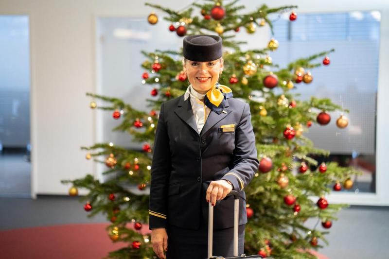 Lufthansa Cabin Crew standing in front of a Christmas tree with a luggage trolley.