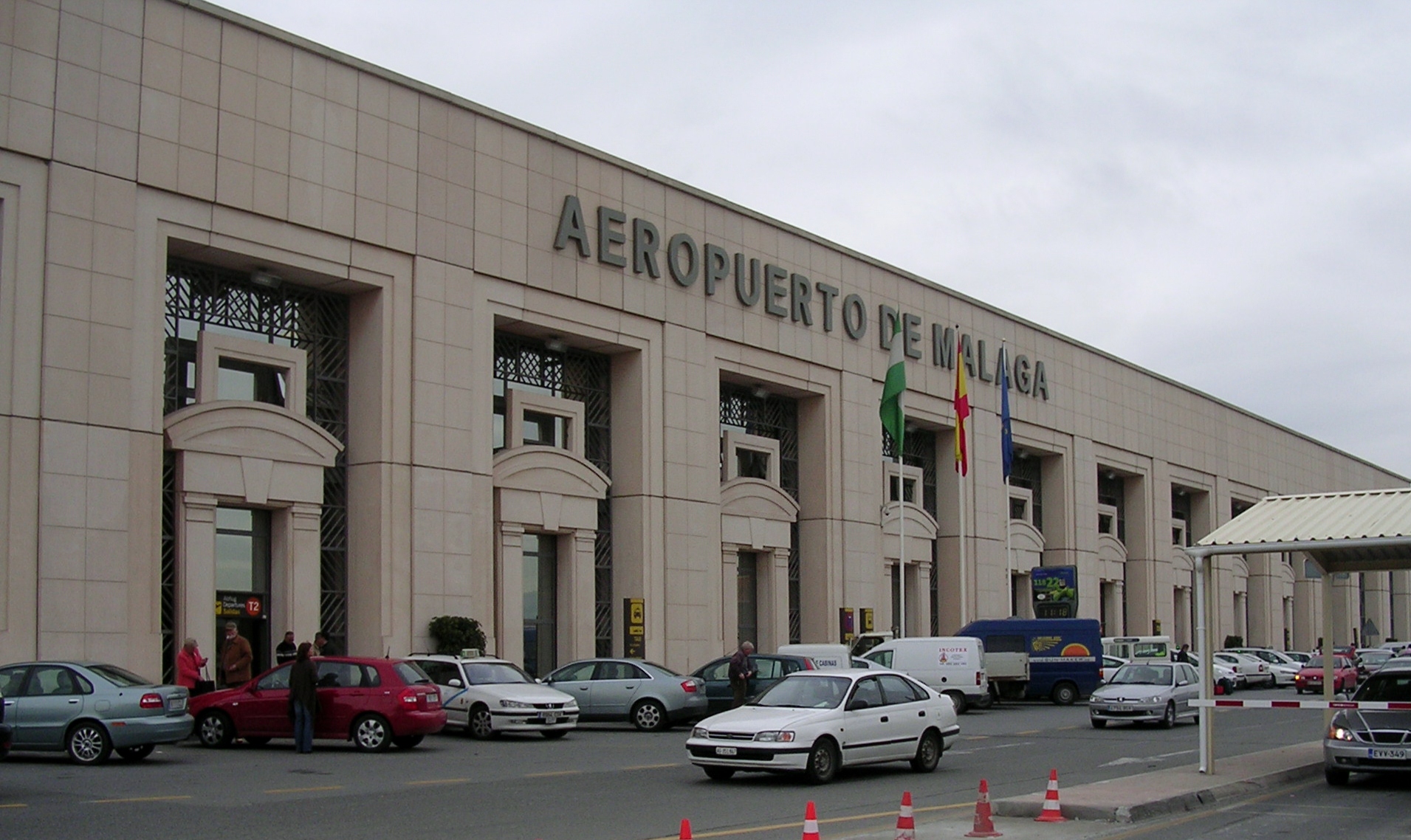 The façade of the Malaga Airport, reading "AEROPUERTO DE MALAGA", with some cars in front.