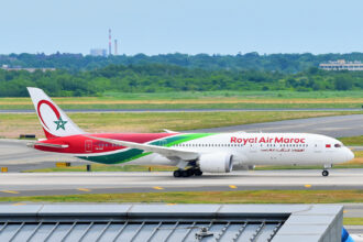 A Royal Air Maroc Boeing 787-9 Dreamliner is rolling for takeoff at John F. Kennedy International Airport, with blue sky.